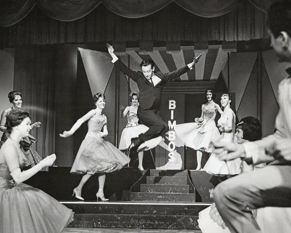 Dean on stage with a line of dancers