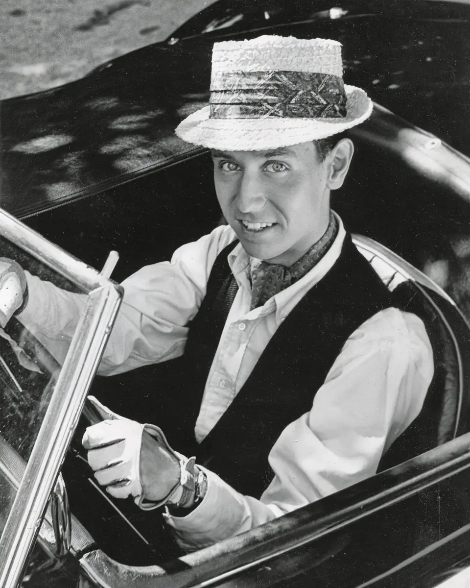 Young Dean in a boater hat, at the wheel of an open car