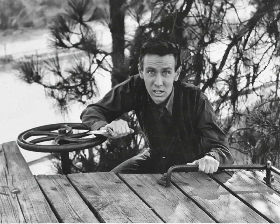 Young Dean climbing onto the wooden roof of a railcar beside a brake wheel, knife in hand