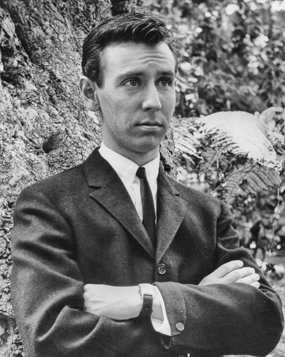 Young Dean in a dark suit and tie, arms crossed